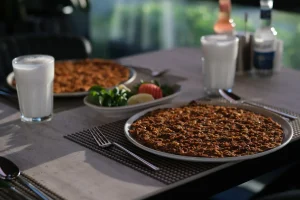 Çakı Restoranda iki tabak lahmacun, ayran bardaklarıyla birlikte bir masada servis ediliyor, yanında yeşillik, limon ve domates dilimleriyle süslenmiş bir tabak var. Kurulum, bulanık bir arka plana sahip iyi aydınlatılmış bir yemek alanında.